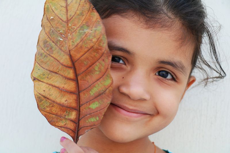 Niña sonriendo detrás de una hoja seca