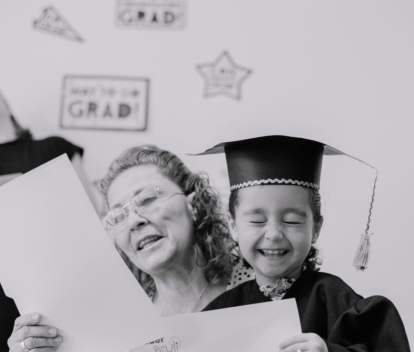 Niña con toga y birrete riendo el día de su graduación, junto a su maestra