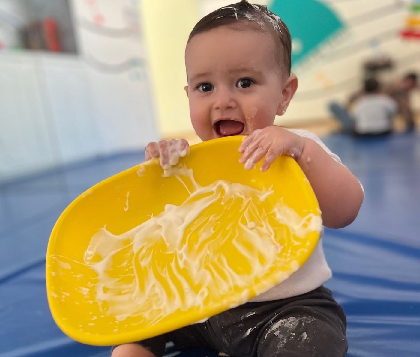 Bebé sonriendo mientras juega con pintura en una charola amarilla